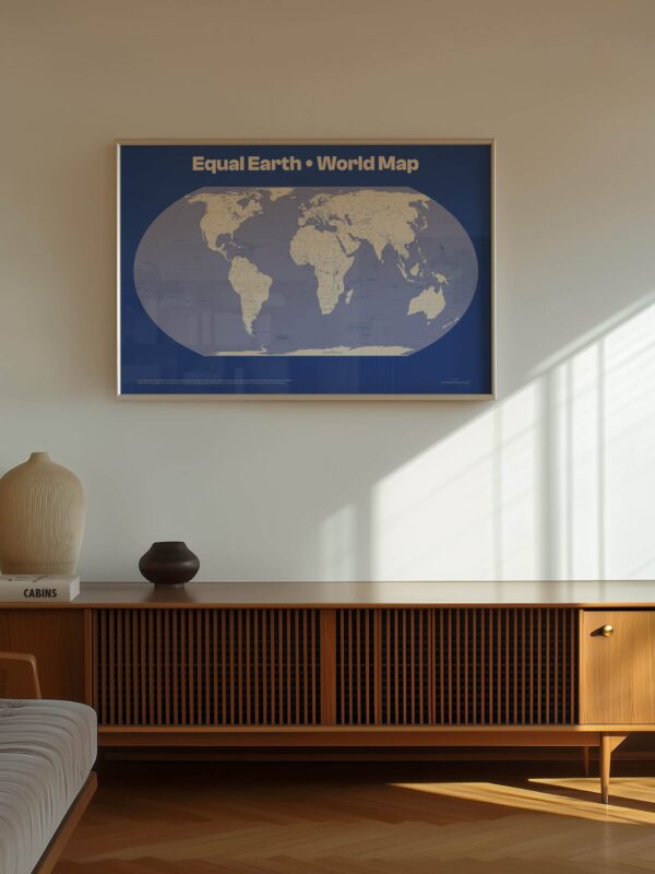 A large wall print of the Equal Earth World Map, framed in a simple design, featuring a blue background and light-colored map projection, displayed above a wooden side table.