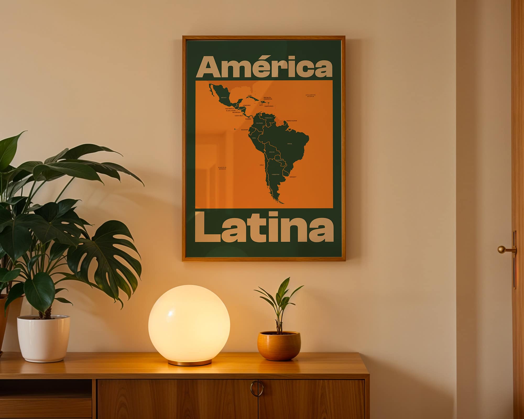 A framed poster titled 'América Latina' featuring a map of Latin America in orange and green colors. Below the poster, a white planter with a green plant and a small brown pot with a plant sit on a wooden surface, next to a round glowing lamp.
