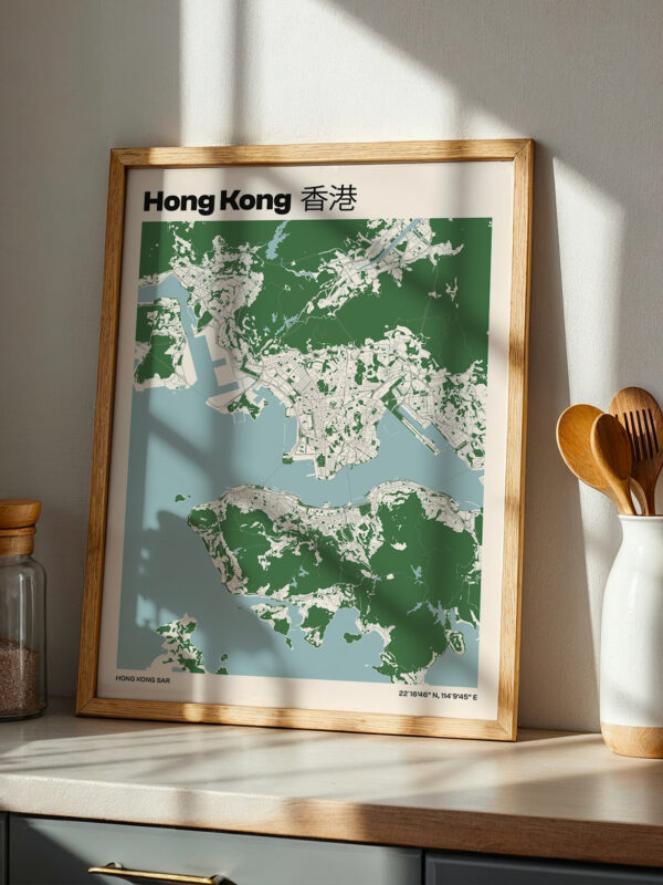 A framed map of Hong Kong displayed on a countertop. The map features shades of green and blue, highlighting the area's topography. In the background, wooden utensils are visible in a white vase, alongside a glass jar.