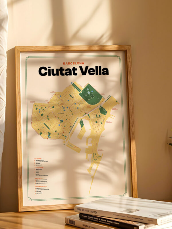A framed map of Ciutat Vella, Barcelona, displayed on a wooden table. The map features streets, parks, and landmarks in a yellow color scheme. Natural light casts shadows from nearby curtains onto the table and wall.